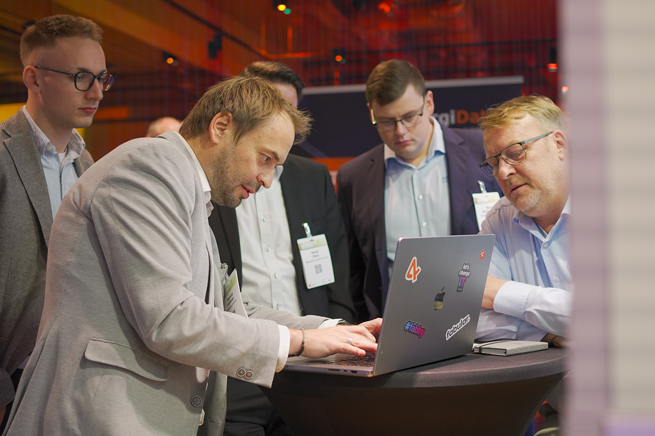 Fünf Männer beim EHI Klima- und Energiekongress 2024 schauen auf einen Laptop
