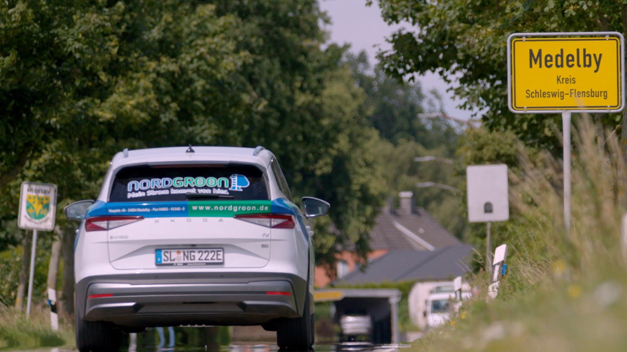 Auto mit Regiogröön-Logo auf Heckscheibe passiert Orstschild von Medelby