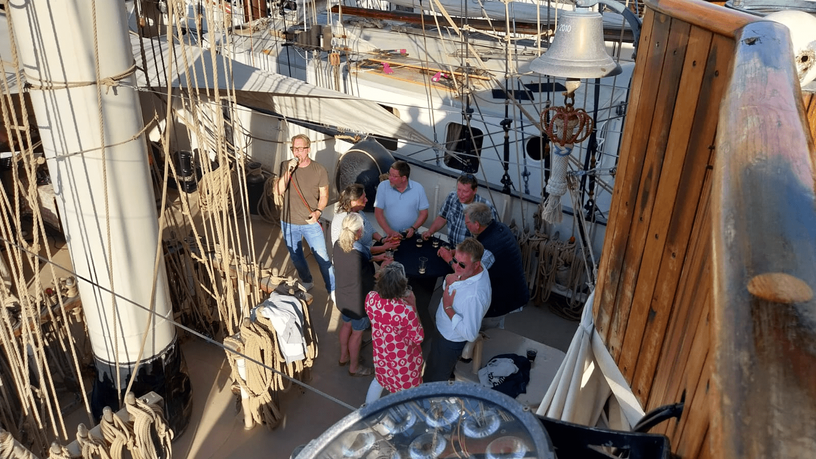 Acht Personen stehen auf Deck eines Segelschiffes, von oben fotografiert