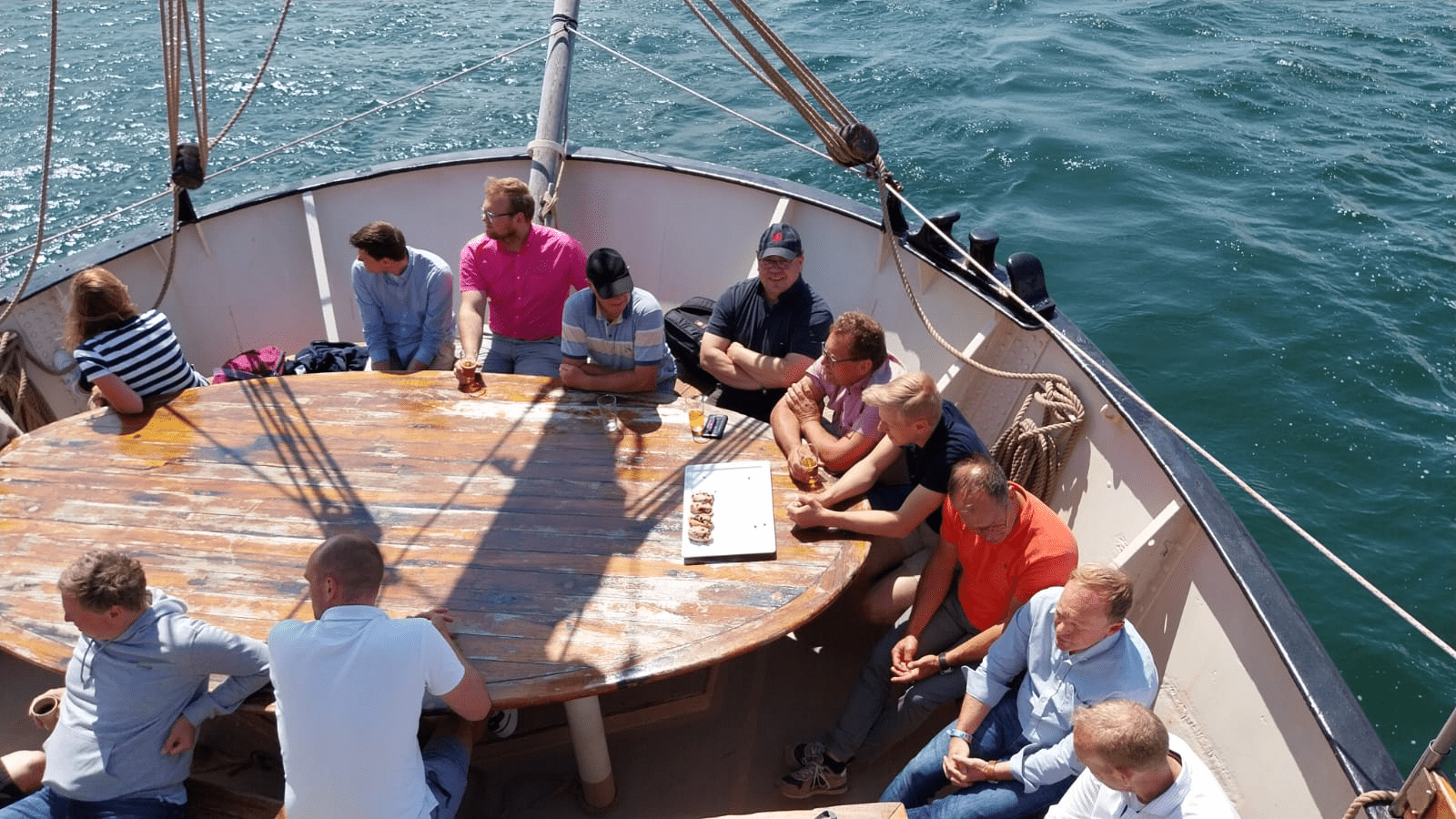 Zwölf Personen sitzem auf einem Segelschiff um einen Tisch herum