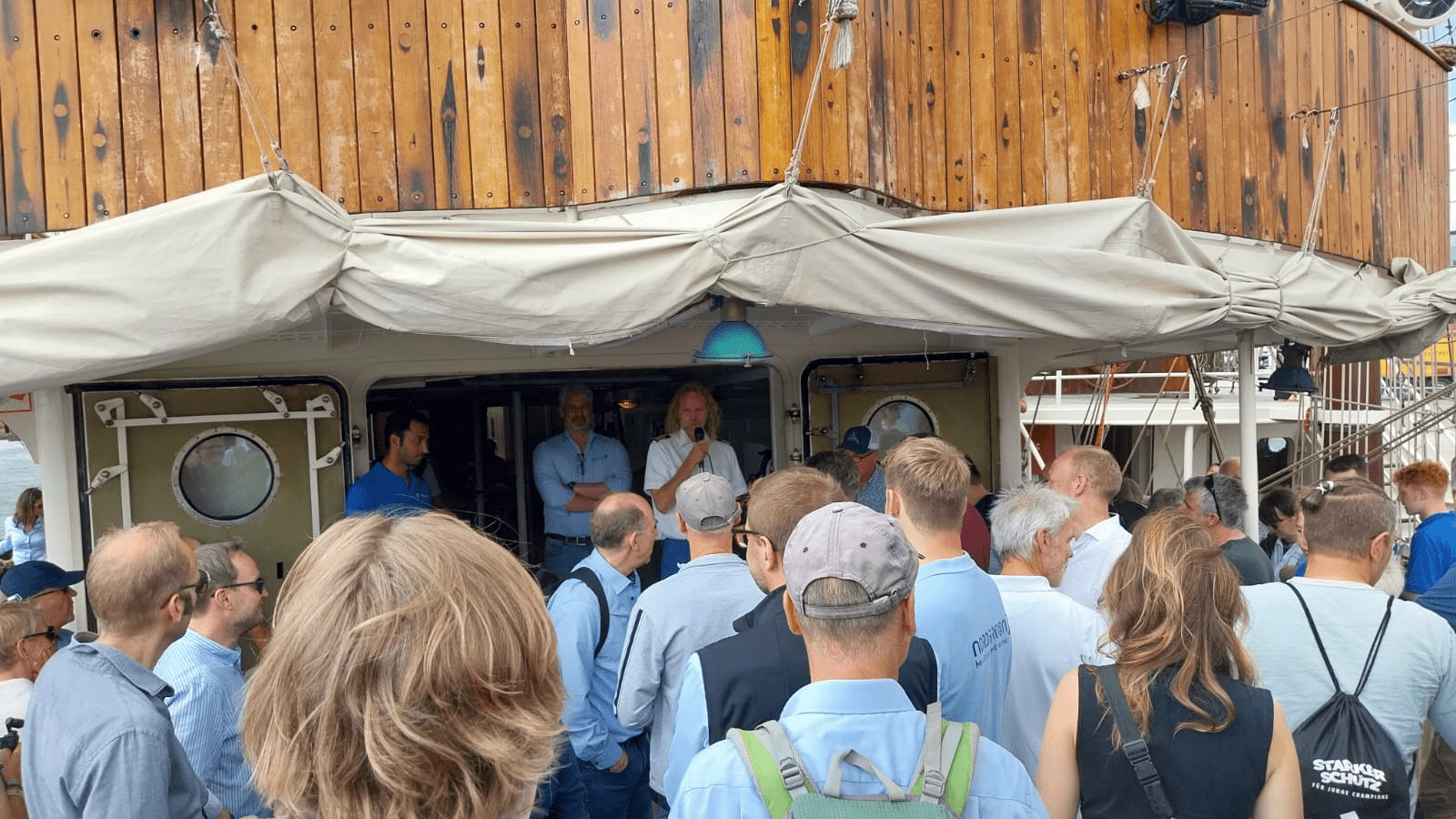 Ansprache auf einem Segelboot, viele Personen lauschen gespannt